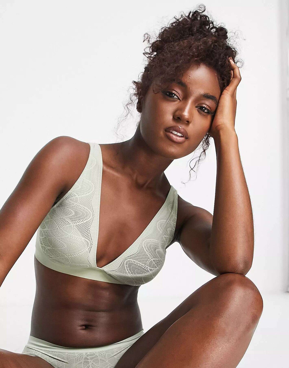 Model wearing a beige lace robe, reclining on a bed.